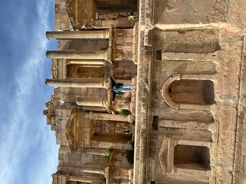       Traveler poses atop the grand stone stage of a Roman temple with tall columns and blue sky above.
  
