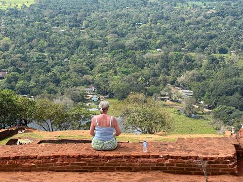       Woman meditates on a weathered brick ledge high above Sri Lanka’s lush plains at Sigiriya.
  