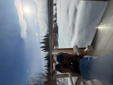       Relaxing view from porch with booted feet up overlooking snowy landscape and pine trees
  