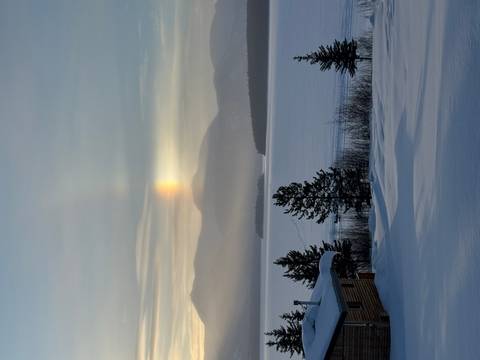       Winter lake with sun dog light phenomenon above distant snowy mountains
  