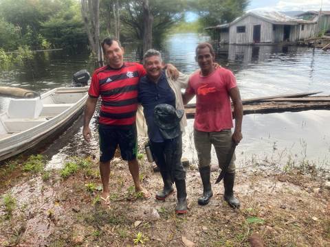       Three men in casual clothes and rubber boots smiling on muddy Amazon riverbank
  