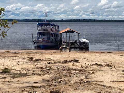       Riverboat anchored at sandy Amazon shore with wooden jetty and vast river view
  