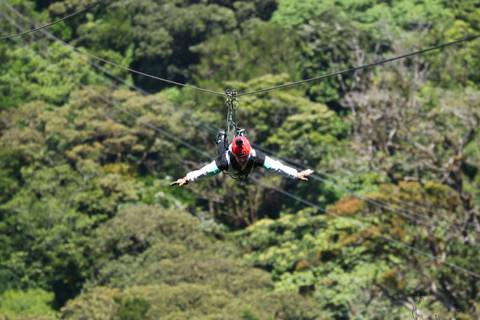       Adventurer in red helmet zip-lining Superman style over lush rainforest canopy
  