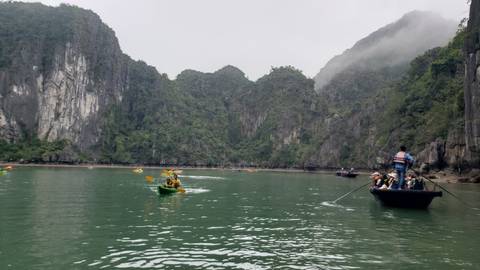       Kayakers paddling emerald waters beneath towering limestone cliffs in misty Ha Long Bay
  
