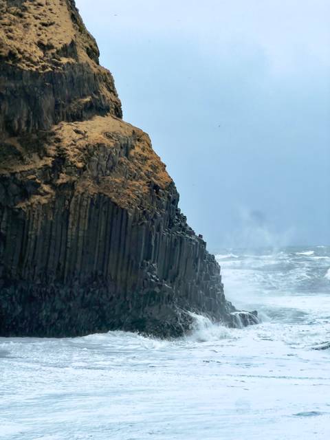       Dramatic basalt column sea cliff battered by crashing North Atlantic waves under grey skies
  