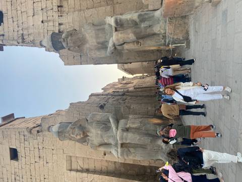       Visitor poses between colossal seated statues at the entrance of Luxor Temple.
  