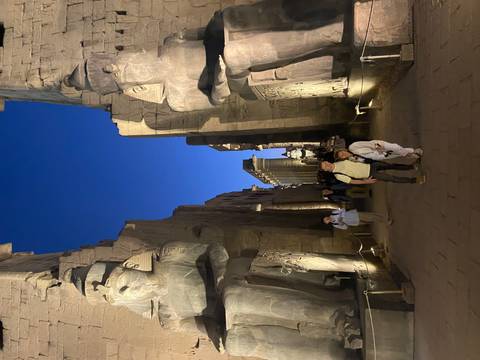       Visitors walk a night-lit avenue of statues at Luxor Temple under a deep blue sky.
  