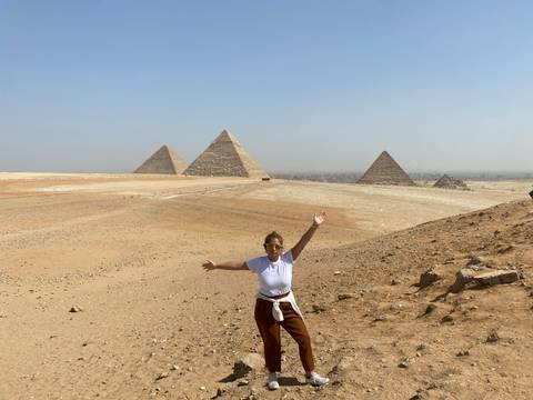       Traveler celebrating in front of the iconic Pyramids of Giza on a clear day.
  