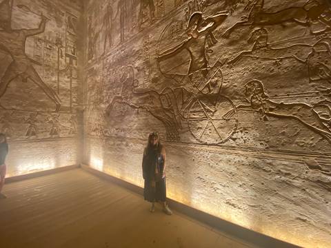       Visitor standing before illuminated wall reliefs depicting ancient Egyptian chariots.
  