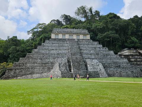       View of the Temple of the Inscriptions pyramid at Palenque with visitors on the lawn.
  