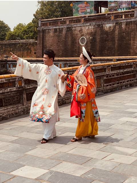       Couple wearing traditional Vietnamese áo dài poses in the imperial citadel courtyard.
  