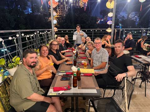       Large tour group enjoys dinner at a rooftop restaurant overlooking city lights.
  
