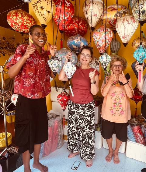       Travelers smile while crafting colorful lanterns inside a workshop.
  