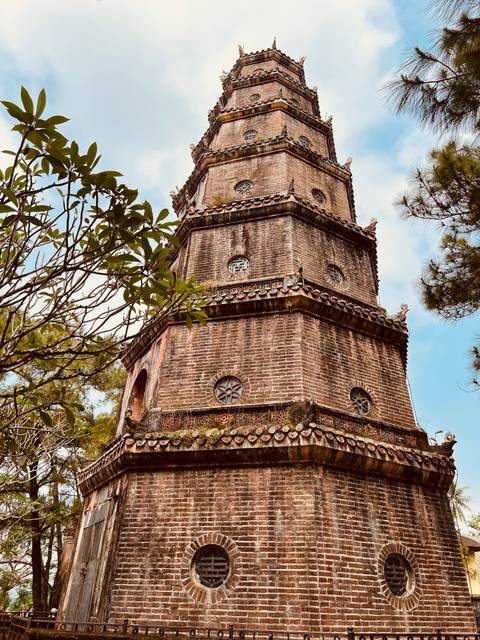       Brick Thien Mu Pagoda tower rises among trees in Hue's serene temple grounds.
  