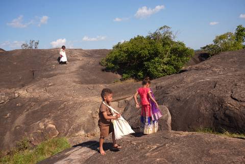       Children in colorful clothing scramble over sun-baked rock formations under a bright blue sky.
  