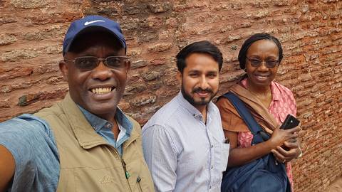       Small group smiling against a rustic brick wall outdoors.
  