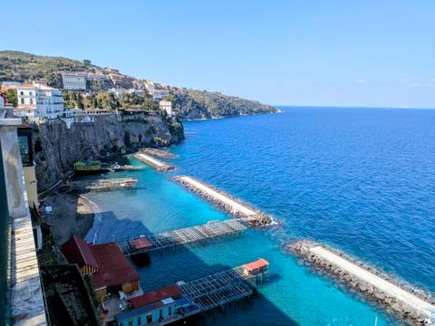       Crystal blue sea with piers and swimming platforms below cliffs of Sorrento’s coastline on a clear day.
  