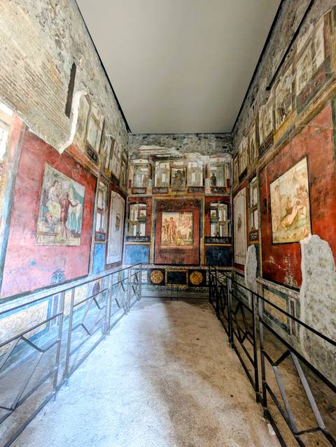       Colorful frescoed room with intricate Roman wall paintings and stone thresholds in Pompeii.
  