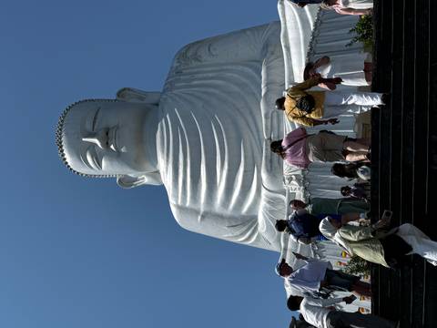       Massive white Buddha statue towers above visitors climbing the steps at Ba Na Hills under clear skies.
  