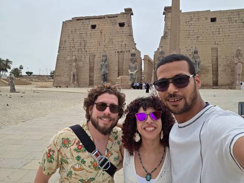       Three friends take a selfie in front of colossal statues and pylons at Luxor Temple.
  