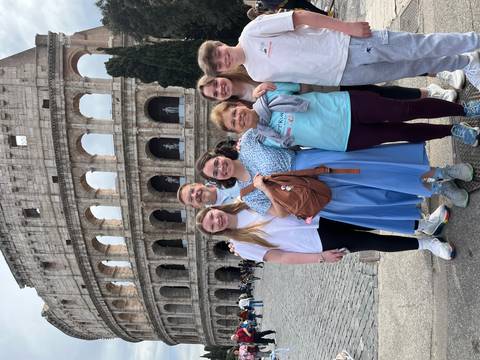       Group posing in front of the Colosseum’s iconic arches on a sunny day
  
