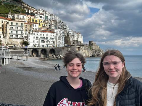       Two friends standing on the beach with the white buildings of Amalfi rising behind them
  