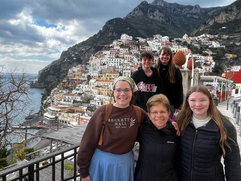      Group of travellers smiling with colorful Positano terraces cascading down the cliff behind
  