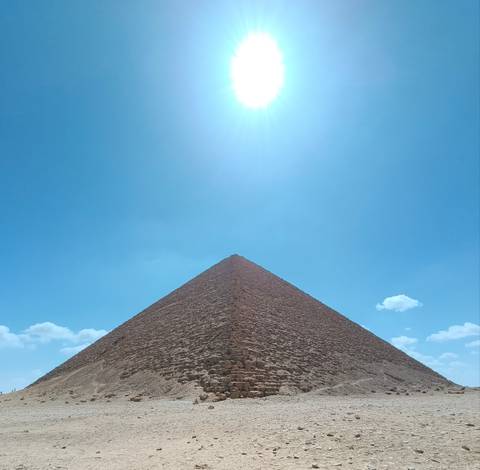       Triangular profile of the Great Pyramid of Giza rising toward a bright noon sun
  