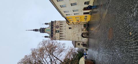       The medieval Clock Tower of Sighișoara rises above a wet cobblestone square on a rainy day.
  