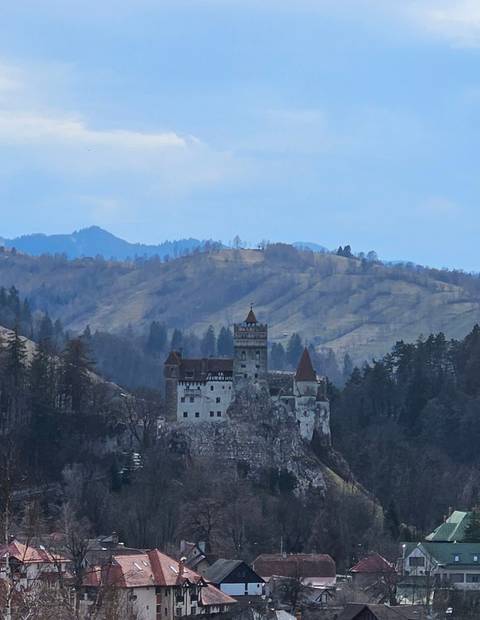       Soft, hazy telephoto shot of Bran Castle against muted mountain slopes.
  