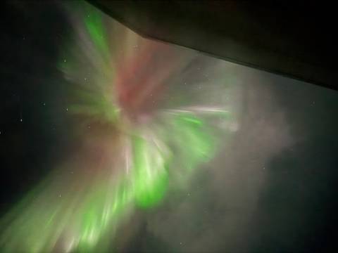       Blurred, abstract view of aurora lights in green and pink streaks against a cloudy night sky.
  
