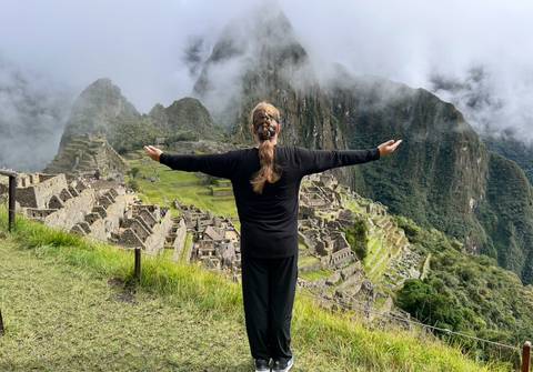       Back-view of a traveller with arms outstretched overlooking the misty terraces of Machu Picchu.
  