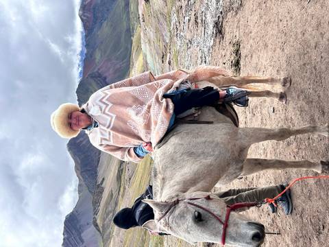       Smiling rider in Andean poncho and furry hat sits atop a horse on a windy high-altitude trail.
  