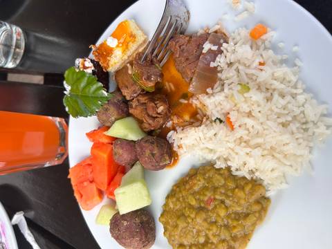       Plate of rice, lentils, stewed meat, fruit and vegetables with a drink in background.
  