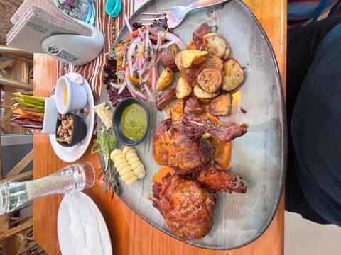       Rustic platter with roasted meat, potatoes, salsa verde, onions and local corn inside a restaurant.
  