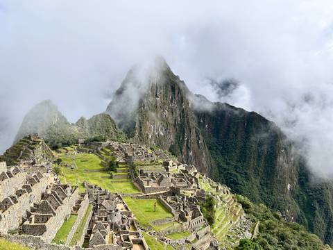       Iconic panoramic view of Machu Picchu ruins perched on a green mountain ridge with clouds drifting around steep peaks.
  