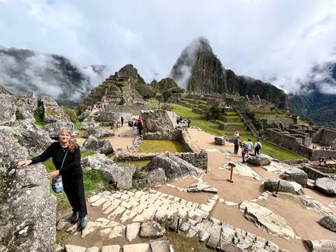       Traveller posing among stone ruins overlooking the full Machu Picchu citadel and surrounding mountains.
  