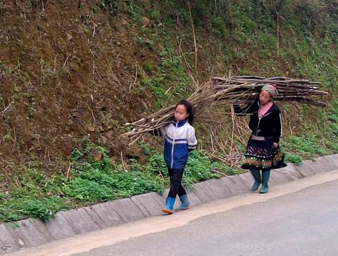      Local woman and child carry bundles of sticks along a rural mountain road.
  