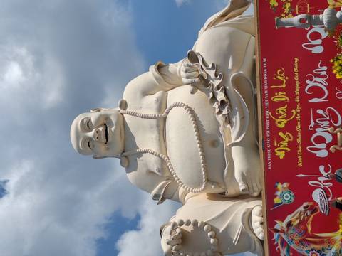      Massive white laughing Buddha statue against a vivid blue sky with red decorative base.
  