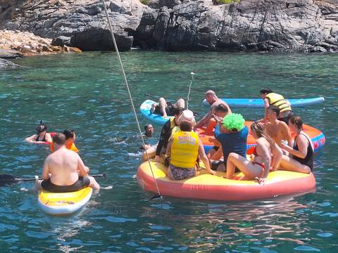       A lively group of travellers on inflatable rafts and kayaks enjoying the turquoise water near limestone cliffs.
  