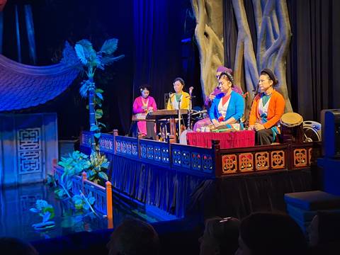       Traditional Vietnamese musicians in colourful attire performing on an indoor stage with instruments.
  