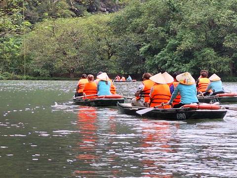       Several small row-boats with visitors in orange life-jackets glide along a lush green river flanked by forest.
  