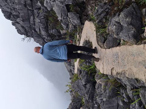       A hiker walks along a narrow stone path through fog-shrouded rocky mountains.
  
