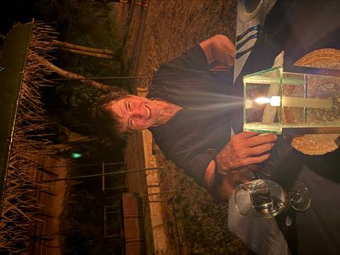       Man seated at an outdoor candlelit dinner table at night, smiling warmly.
  