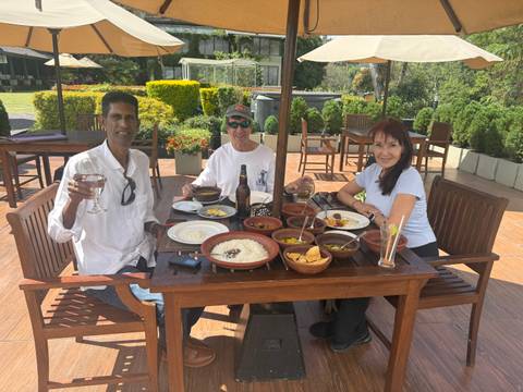       Three diners enjoying a traditional Sri Lankan meal on a sunny patio surrounded by gardens.
  