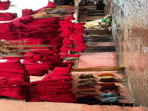       Bundles of bright red dyed wool hanging to dry in a narrow Marrakech alleyway
  