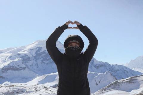       Trekker in winter gear forming a heart shape with hands against snowy Annapurna massif
  