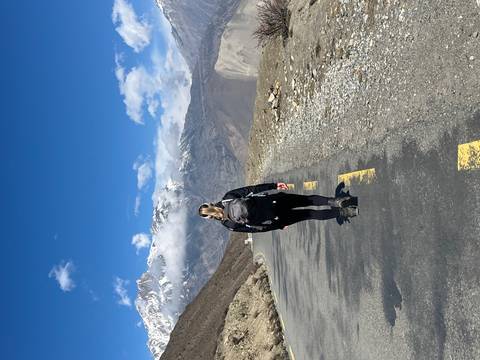       Female trekker walks along a mountain road flanked by barren slopes and snow-capped peaks
  
