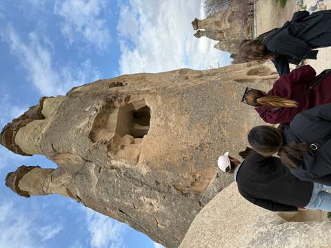       Travellers gaze up at a fairy chimney rock formation with carved cave openings in Cappadocia
  