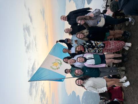       Hiking group celebrates at dawn with a Guatemalan flag on a volcanic summit above the clouds.
  